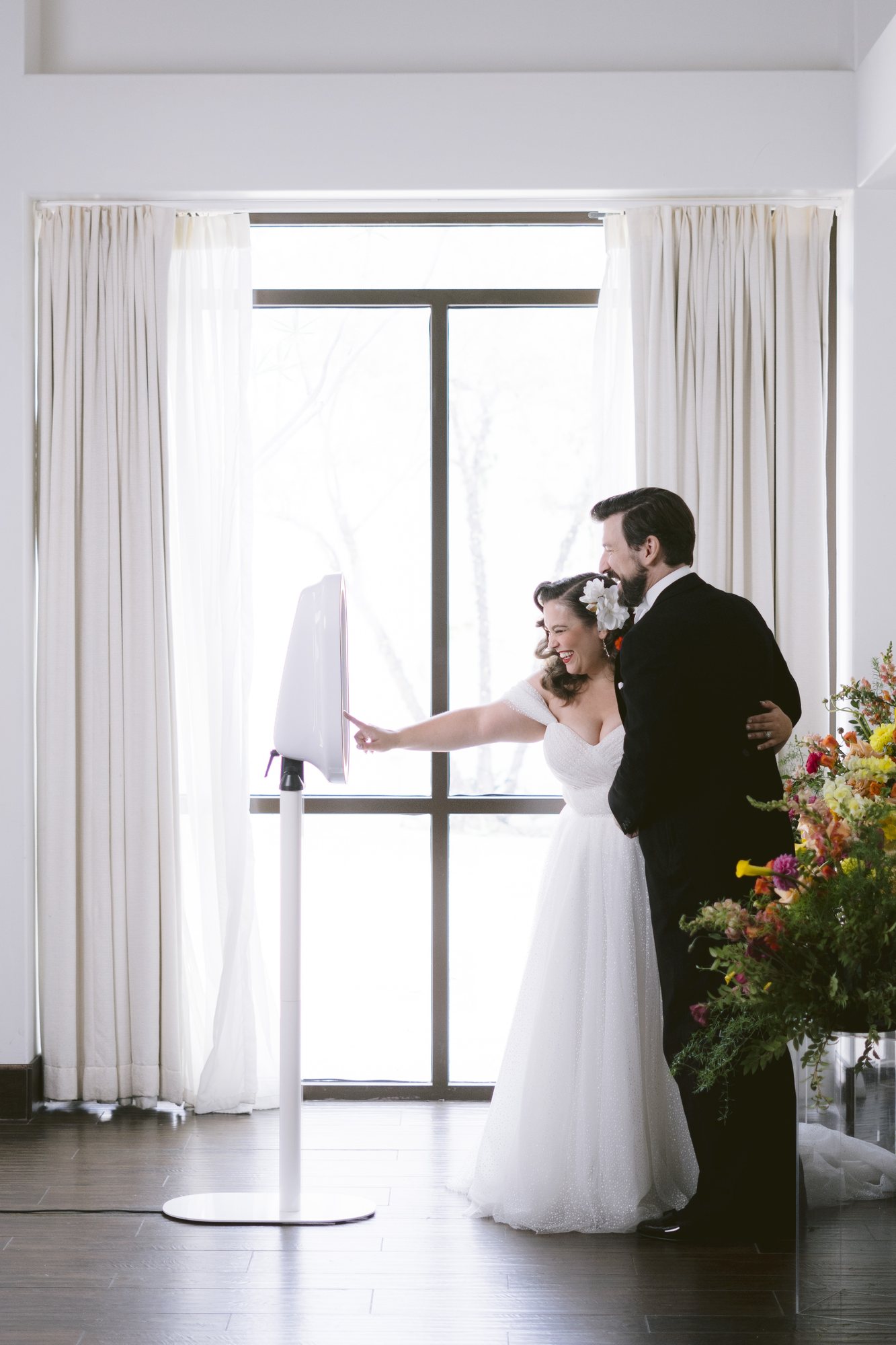 A bride and groom at the booth beside a bright window hung with white curtains
