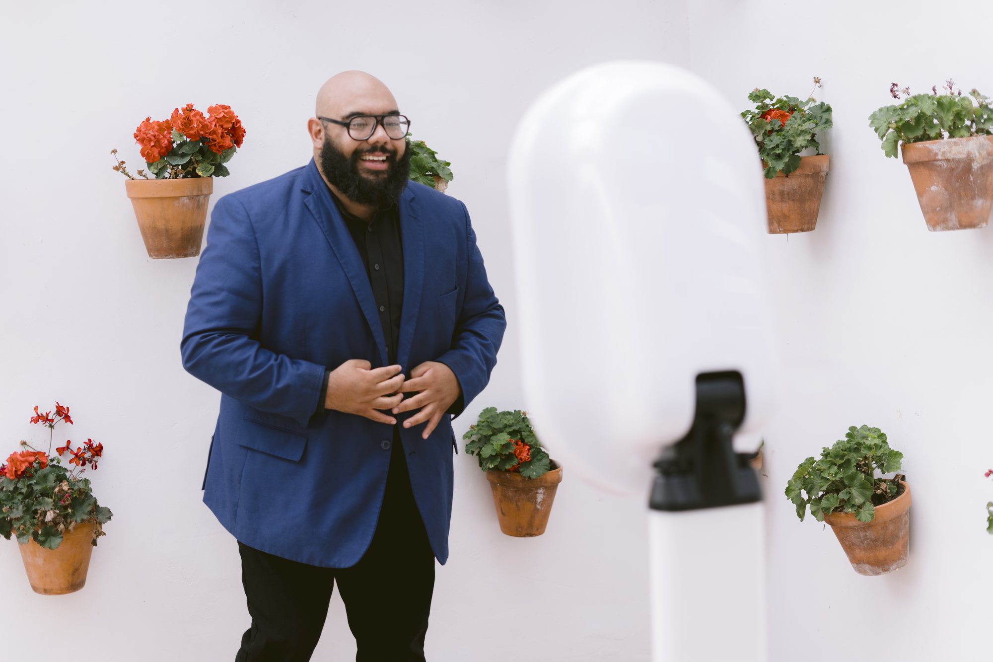 A guest in a blue blazer and glasses laughing beside the booth, potted geraniums on the white wall