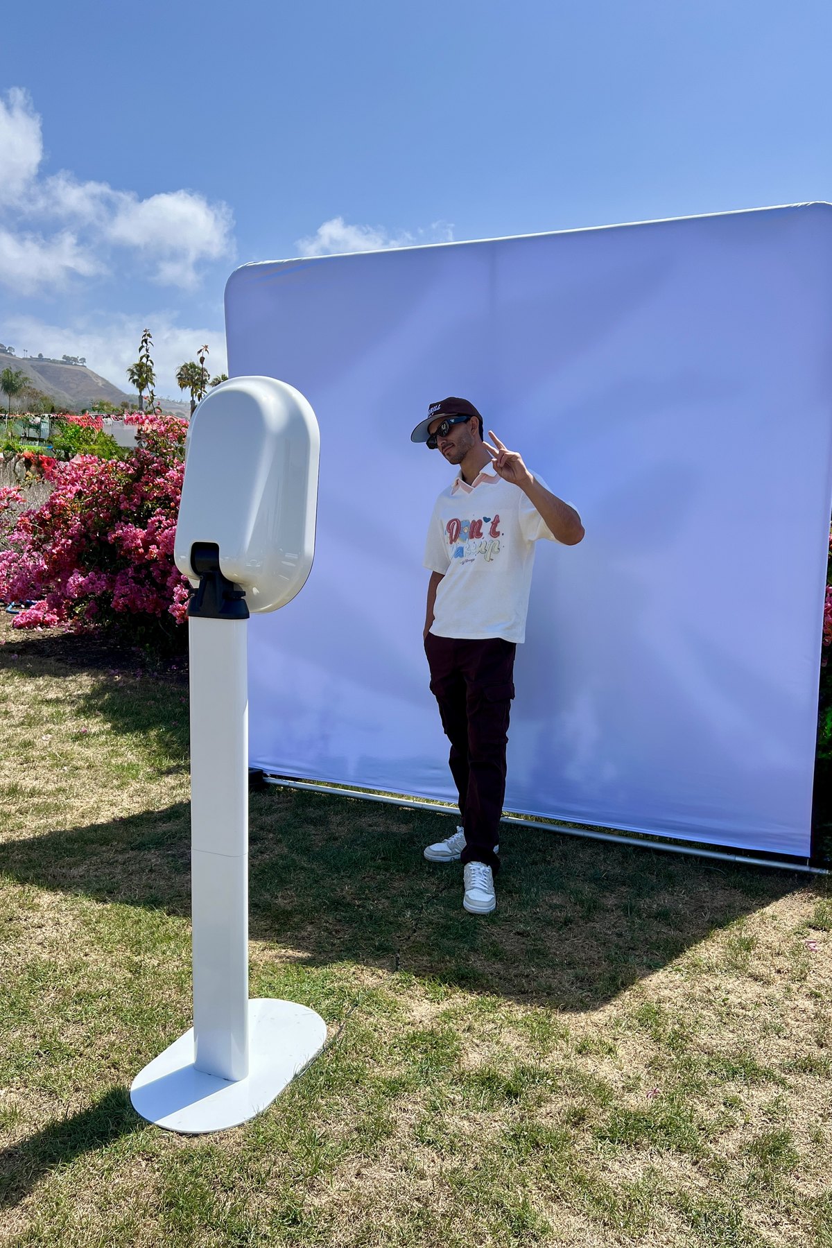 A guest in a cap flashing a peace sign in front of a backdrop on a lawn beside a white booth