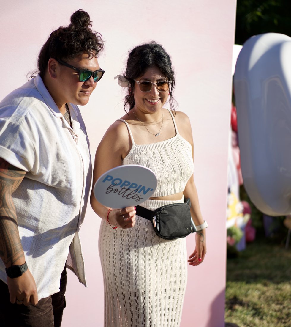 Two guests holding a prop sign beside the booth at an outdoor event