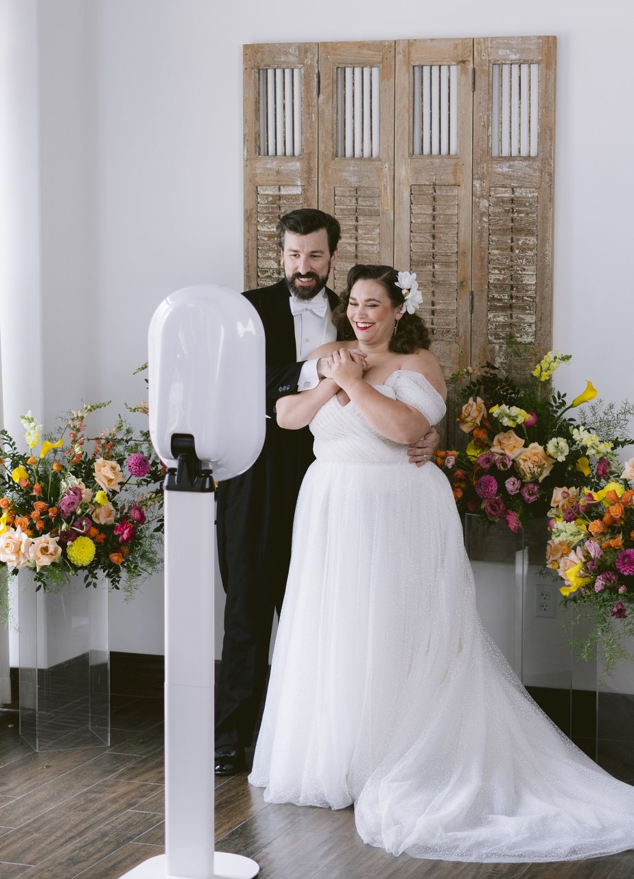 A bride and groom at the photo booth in front of carved wood doors and bright florals