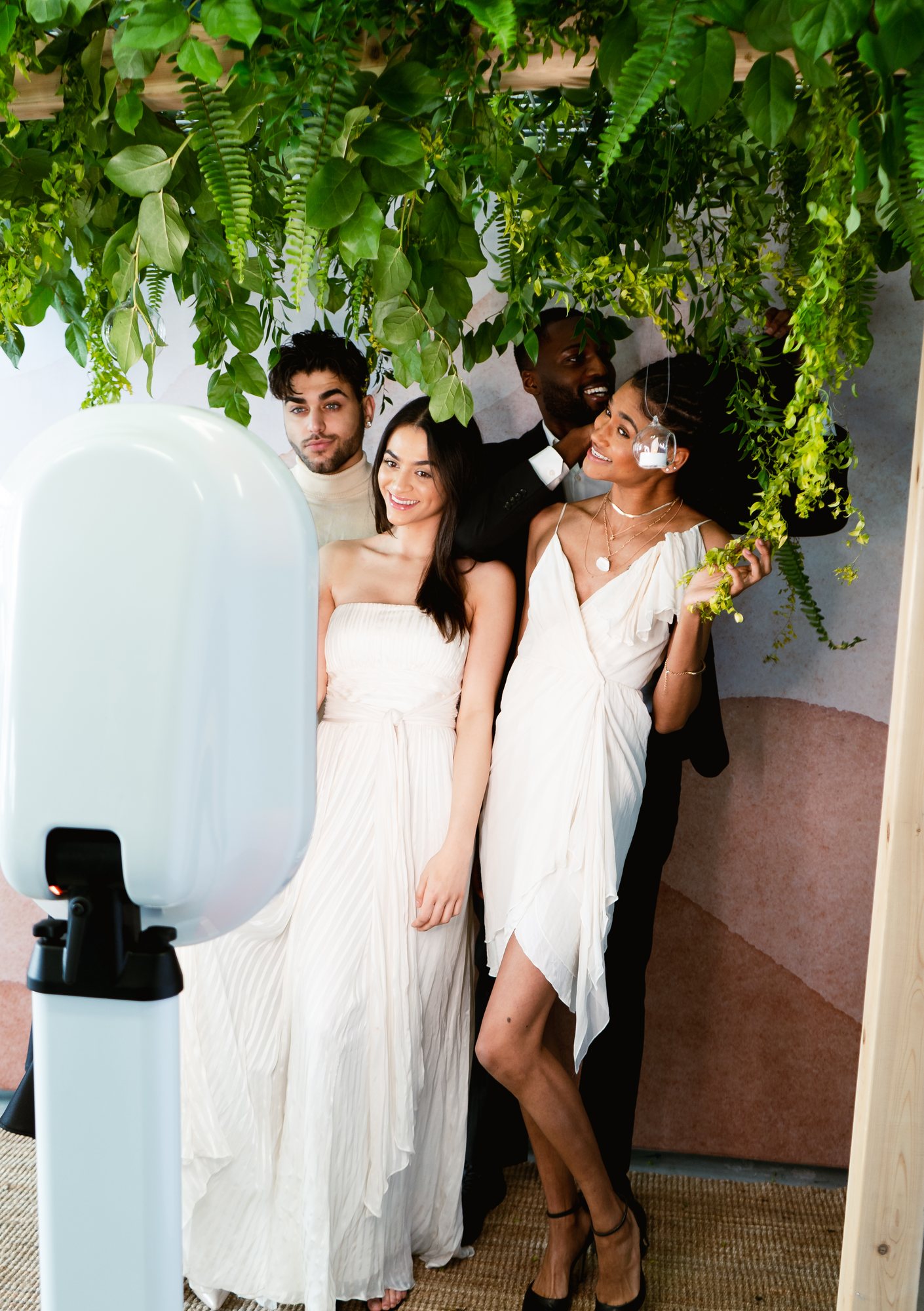 A wedding party dressed in white posing together under hanging greenery